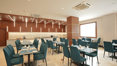 Restaurant at Pride Elite Mandarmani with teal upholstered chairs at laid dining tables, a wood-slat feature ceiling, and a buffet counter with chafing dishes.