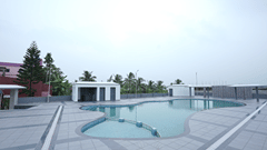Rooftop pool at Pride Elite Mandarmani seen from a distance, with a tall conifer tree, palms, and neighbouring buildings on the skyline.