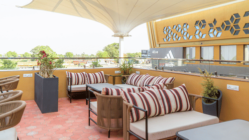 The bright rooftop lounge at Pride Elite Himmatnagar features striped sofas under a large canopy tent shield.