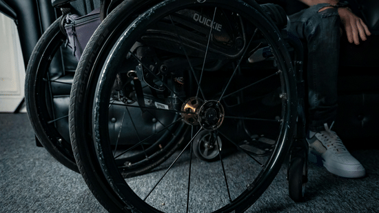 A close-up view focusing on the large wheel and frame of a manual wheelchair parked on a carpeted floor.