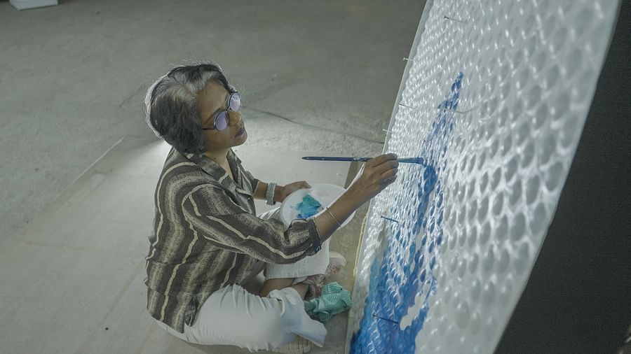 A woman is painting on a large bubble-wrap surface, focused on creating a blue design.