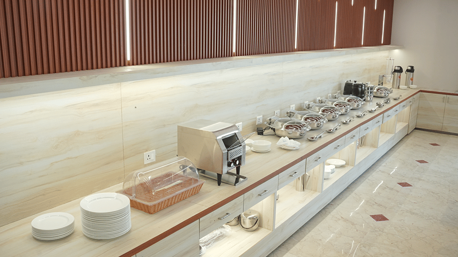 Buffet counter at Pride Elite Mandarmani with stacks of white plates, a bread basket, a toaster, and a row of covered chafing dishes with serving spoons.