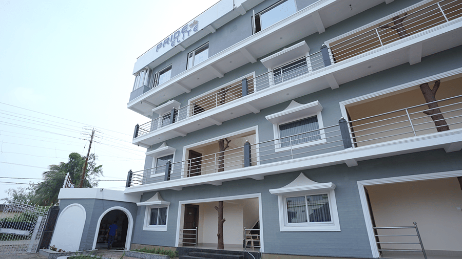 Exterior of Pride Elite Mandarmani with the Pride Elite signage, grey and white multi-storey facade, balconies with decorative tree sculptures, and a gated entrance.