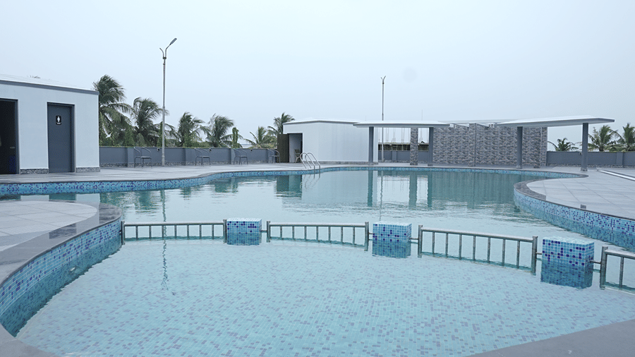 Close angle of the rooftop pool shallow end at Pride Elite Mandarmani with mosaic tiled steps, a railing, and washroom cabana in the background.
