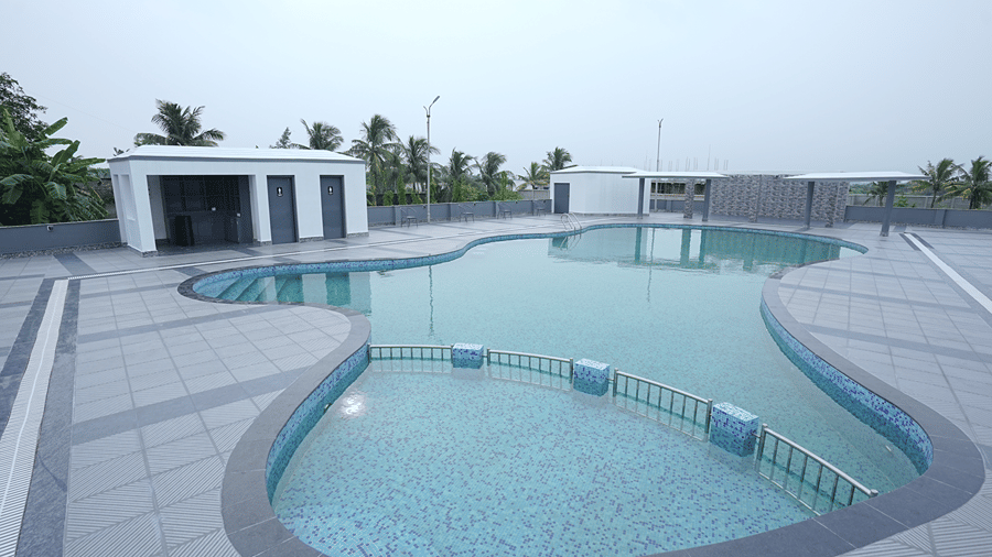 Elevated view of the freeform rooftop pool at Pride Elite Mandarmani with a shallow railed section, washroom block, and banana leaves in the corner.