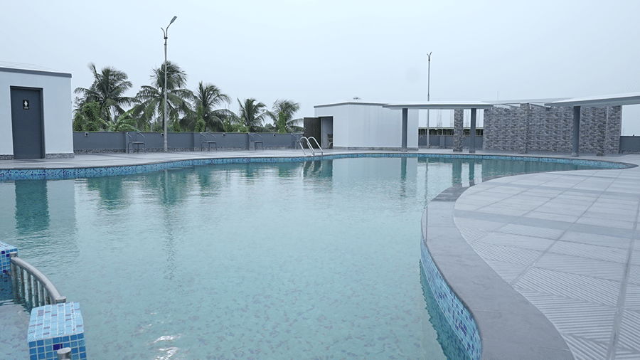 The main section of the rooftop pool at Pride Elite Mandarmani with a ladder handrail, wide tiled deck, and palm trees beyond the boundary wall.