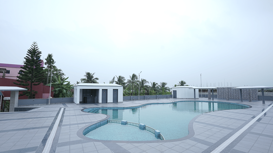 Rooftop pool at Pride Elite Mandarmani seen from a distance, with a tall conifer tree, palms, and neighbouring buildings on the skyline.