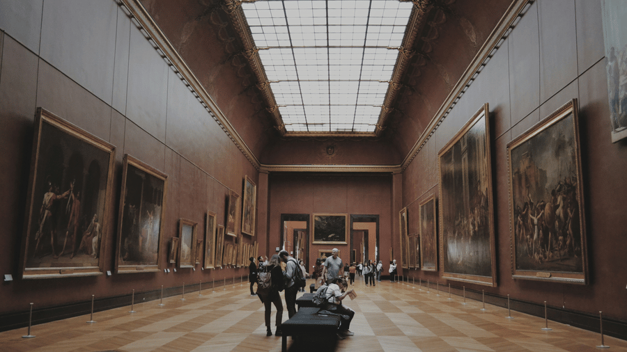 Grand museum gallery with classical paintings displayed along tall walls.