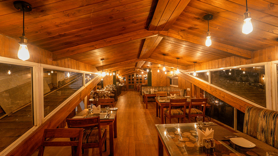 An image of the restaurant featuring chairs, tables, and bright lights, set up in its wooden interiors - DLS Whispering Winds