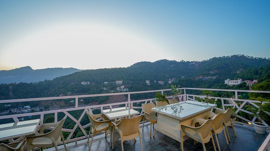 An image featuring the view of mountains from the terrace with chairs and tables - DLS Whispering Winds