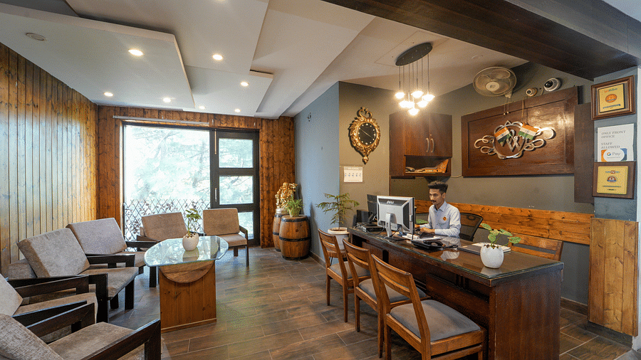 The reception area of DLS Whispering Winds showcasing the reception desk where a receptionist is working, and also featuring chairs, sofas, and a table