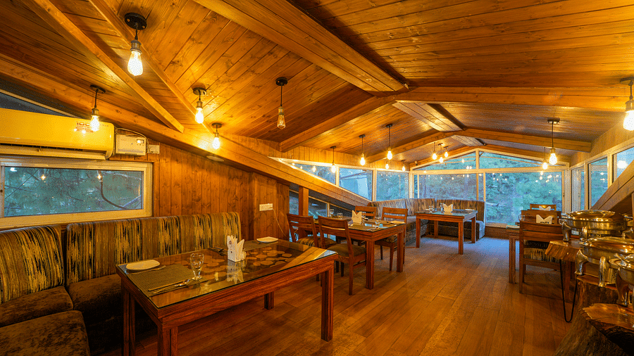 The wooden interior of Ruttba at DLS Whispering Winds with chairs and tables with a view from the glass windows