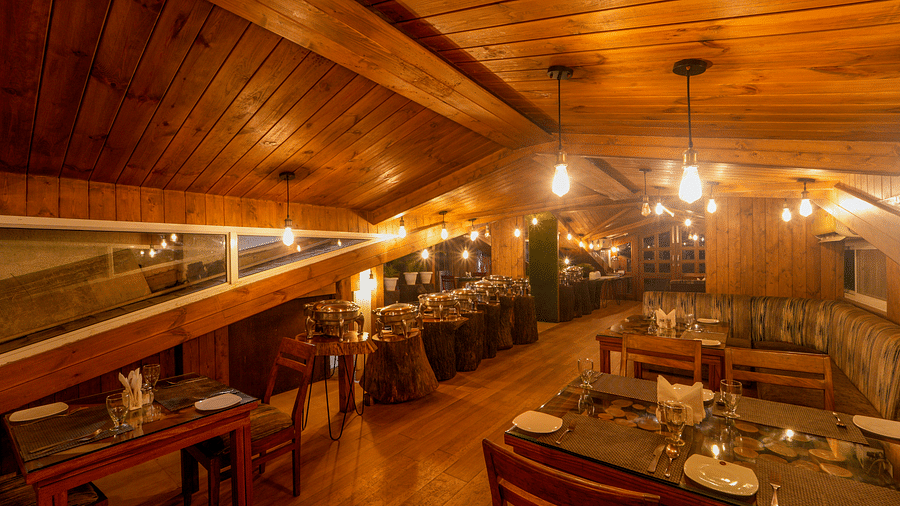 The wooden interiors of the restaurant at DLS Whispering Winds with chairs and tables which it lit with bright lighting