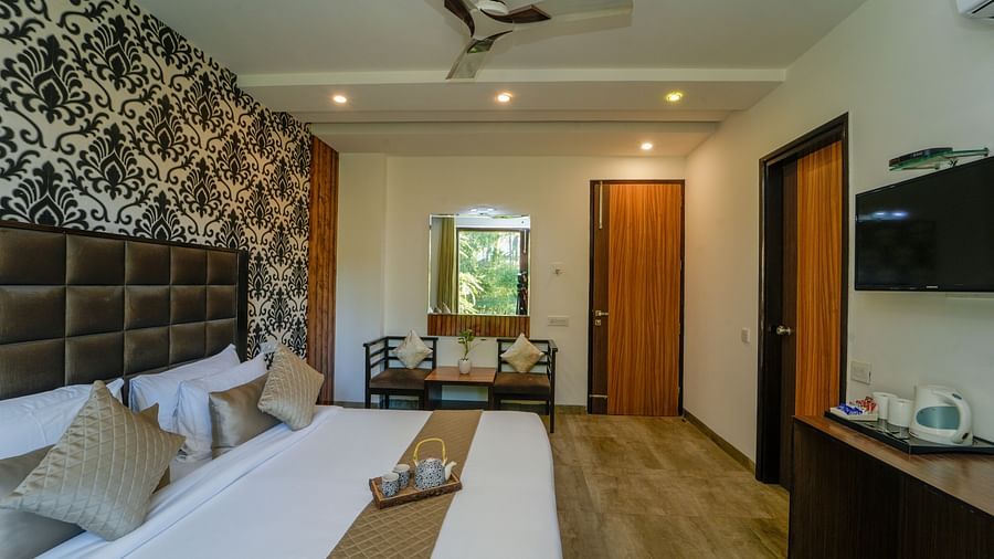 An image of the deluxe room with a bed, chairs and table, flat screen TV, and other room amenities - DLS Whispering Winds