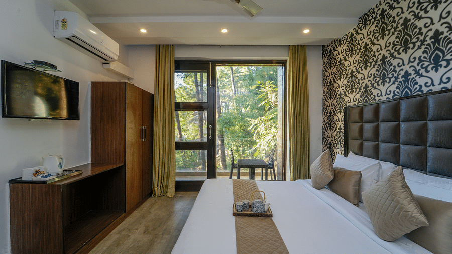 The deluxe room with a bed, a flat screen TV, an air-conditioner, and the glass door leading to the balcony with forest view - DLS Whispering Winds