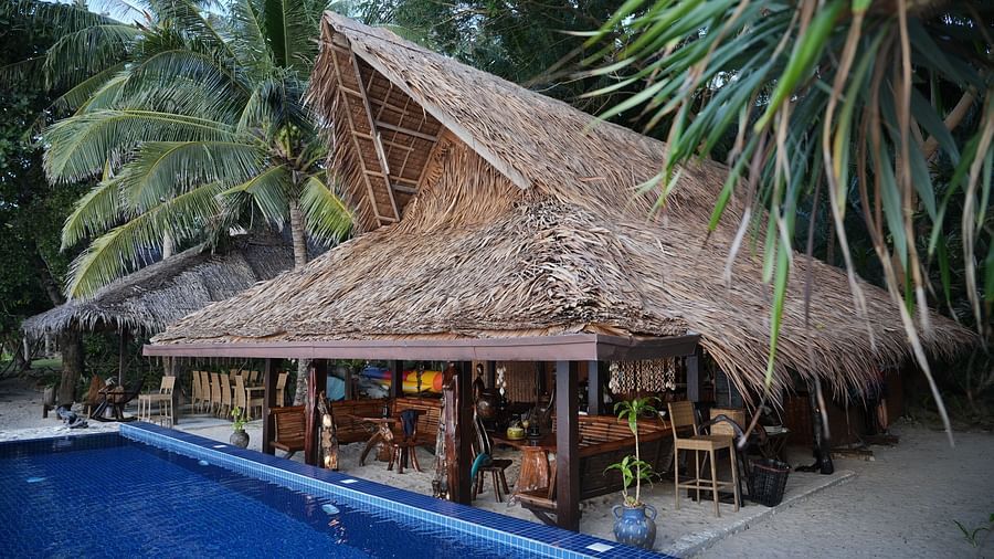 Thatched-roof restaurant by the pool surrounded by palm trees at Flower Island Resort.