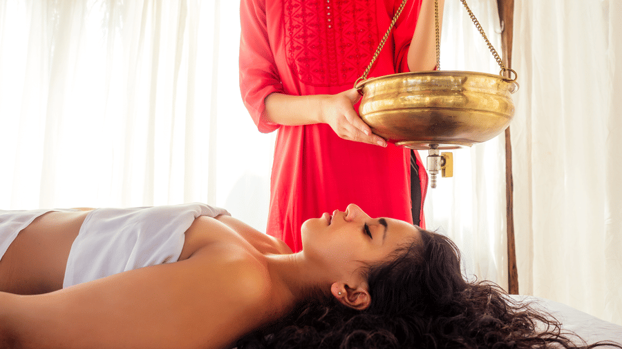 Woman receiving an Ayurvedic oil treatment on her forehead.