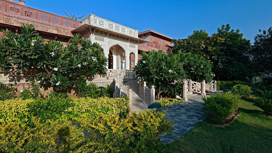 A medieval haveli with open courtyards, verandahs, and intricate stone work surrounded by lush greenery - Khas Bagh, Jaipur