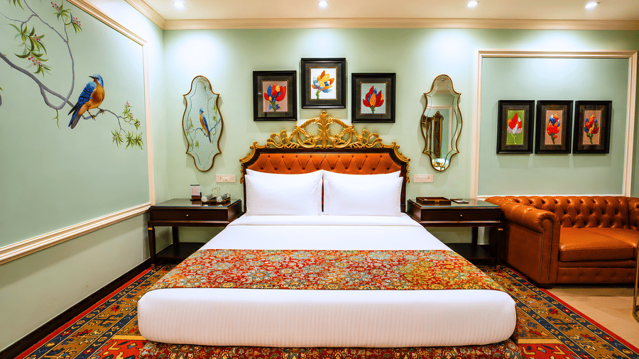 Deluxe room with a king bed, carved headboard, a leather sofa, framed floral artwork and a hand-painted bird mural at MAYFAIR Oasis Resort & Convention, Jharsuguda.