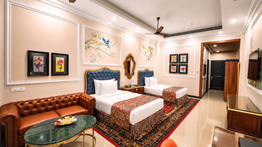 Executive room with two single beds, blue headboards, a leather sofa, framed floral art and painted bird murals at MAYFAIR Oasis Resort & Convention, Jharsuguda.