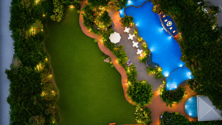 Aerial evening scene of a manicured lawn, a freeform pool with parasols and a gazebo bordered by trees at MAYFAIR Oasis Resort & Convention, Jharsuguda.
