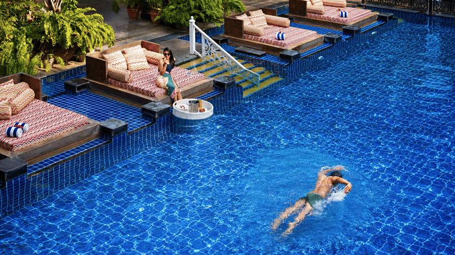 Guest swimming in a large outdoor pool lined with sun loungers at MAYFAIR Palm Beach Resort, Gopalpur-on-Sea.