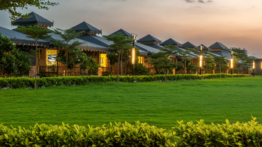 The accommodation blocks of Pushkara Resort & Spa, Ajmer, with cottage style roofs and warm lighting seen from the lawn.