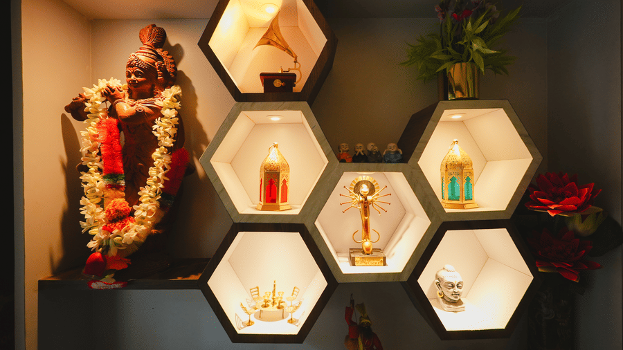 An illuminated wall display featuring honeycomb hexagonal shelves showcasing trophies, decor items, and a garlanded statue.