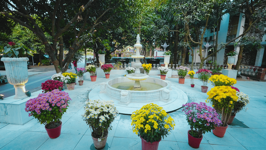 A white stone fountain in a resort courtyard, surrounded by neat rows of colourful potted flowers.