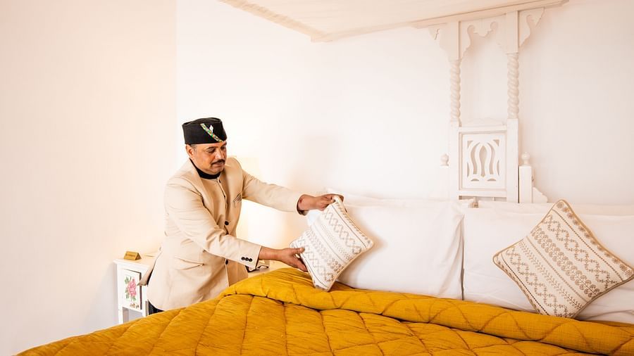 A man arranging pillows on a bed at Te Aroha By Shervani, Mukteshwar
