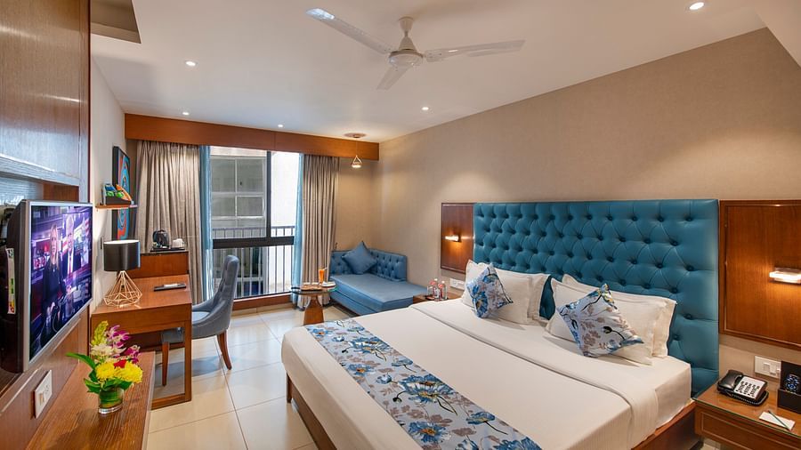 A bright hotel room with twin beds, a seating area, and a television - SK Lords Inn Ahmedabad