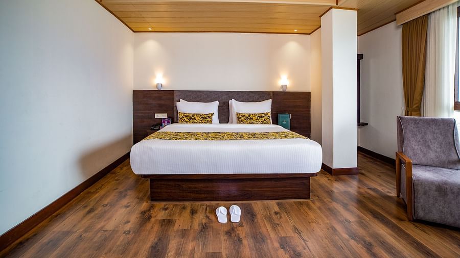 A neatly made double bed in Sumitel hotel with a designed pillow, a pair of sandals on the floor,  matching wooden flooring and ceiling.