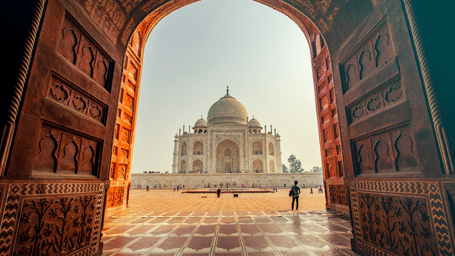 Ornate Mughal gateway framing a symmetrical view of the Taj Mahal and its marble courtyard in Agra.