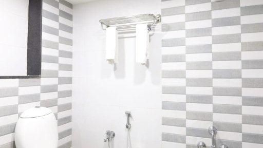 A brightly lit interior of a modern bathroom at Pravasa Ahmedabad featuring a commode along with the shower area beside it.