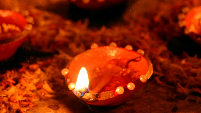 Diyas or traditional lamps lit in a row surrounded by flower petals