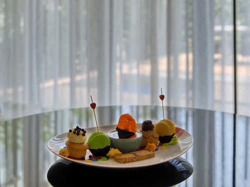 A plate of dessert with delicious macaroons and cup cakes with frosting over it kept on a table at Azaya Beach Resort, Goa.