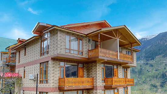 Facade of Clarks Inn Suites in Manali with lawn surrounding the bulding under clear blue sky with mountains in the background