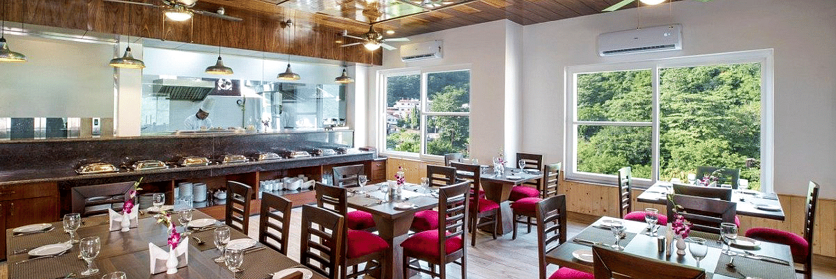 Full view shot of the restaurant at Regenta Inn DLS with neatly arranged dining tables with ample of natural lighting inside.