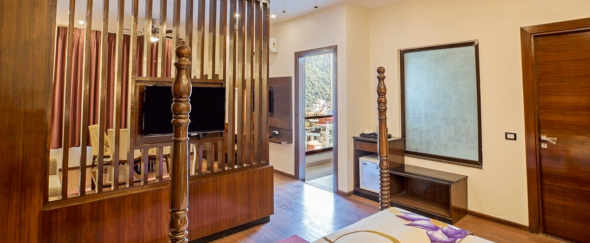 A television mounted on the wooden partition along with a translucent square window on the bathroom wall at Regenta Inn DLS.