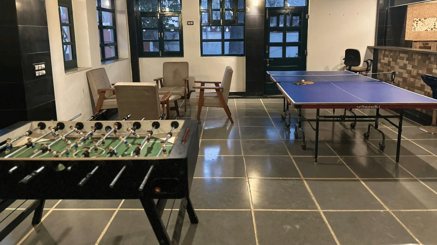 A recreation room featuring a foosball table in the foreground, seating areas, and a blue ping pong table in the back at Amantra Shilpi Resort, Udaipur.