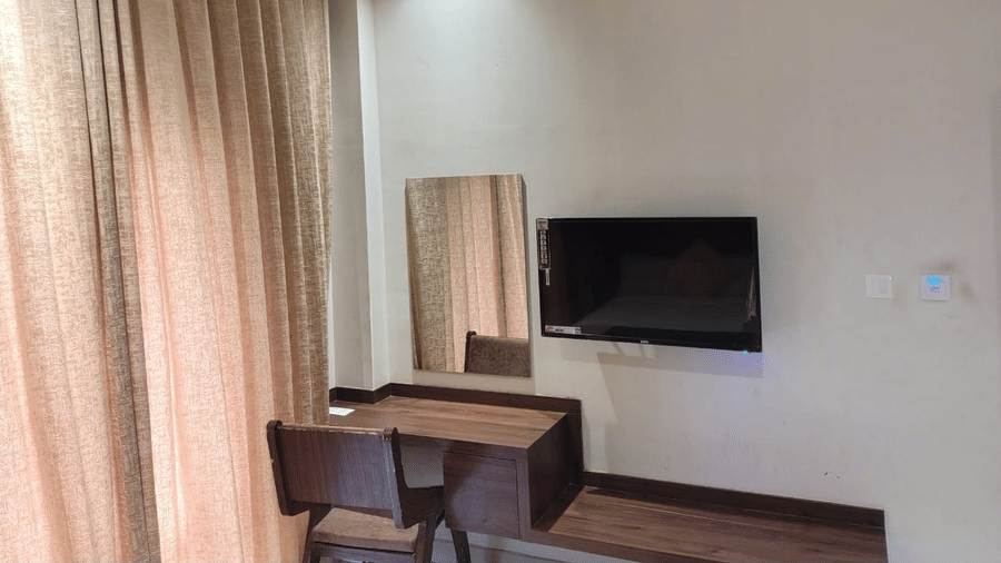 Workstation at Lawn View Room at Cholaa Dynasty, Kumbakonam featuring a working desk with chair, a  flat TV screen, and a mirror next to it. 
