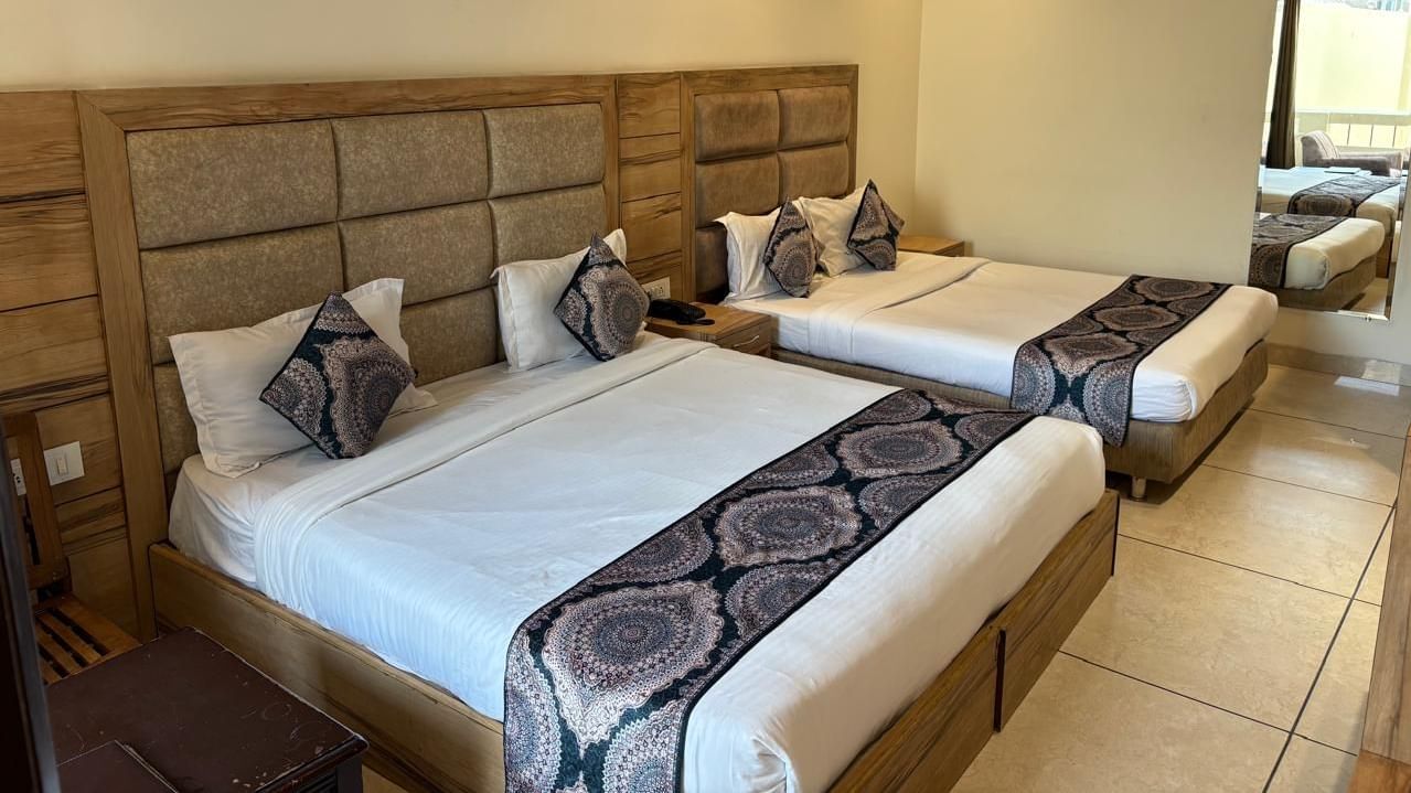 A hotel room featuring two beds side by side, each with a striped bedspread, and a small painting on the wall.