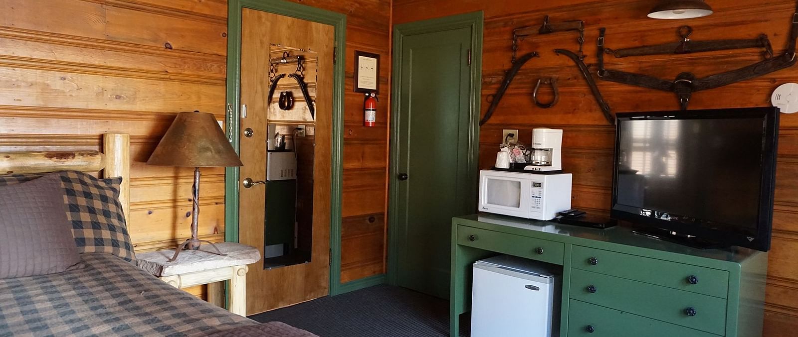 A room at Shaver Lake Village Hotel with a double bed, a lamp on a night stand, a green cabinet and wooden paneling throughout.