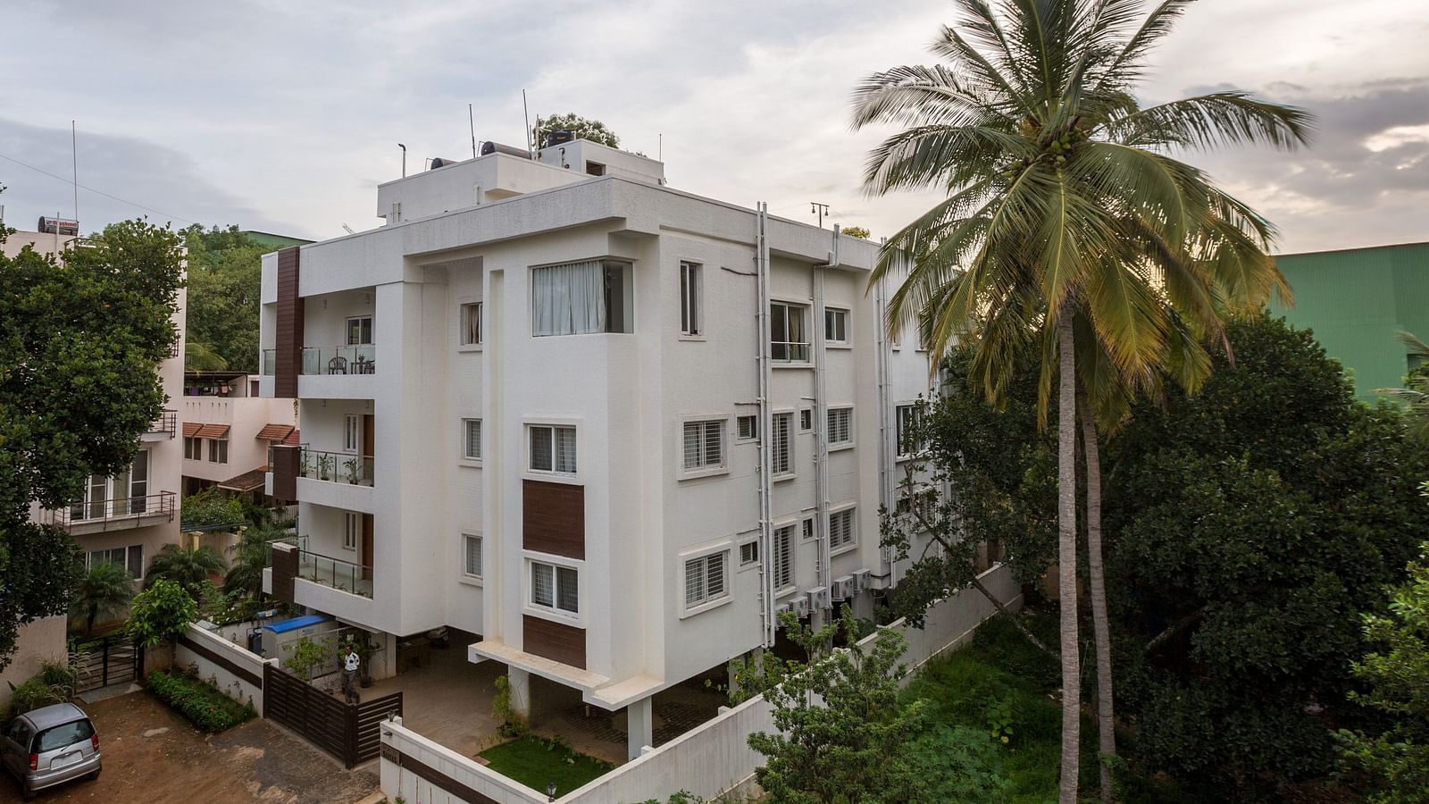 A light-coloured building exterior surrounded by green trees under a bright sky - Sanctum Suites BEL Road, Bangalore