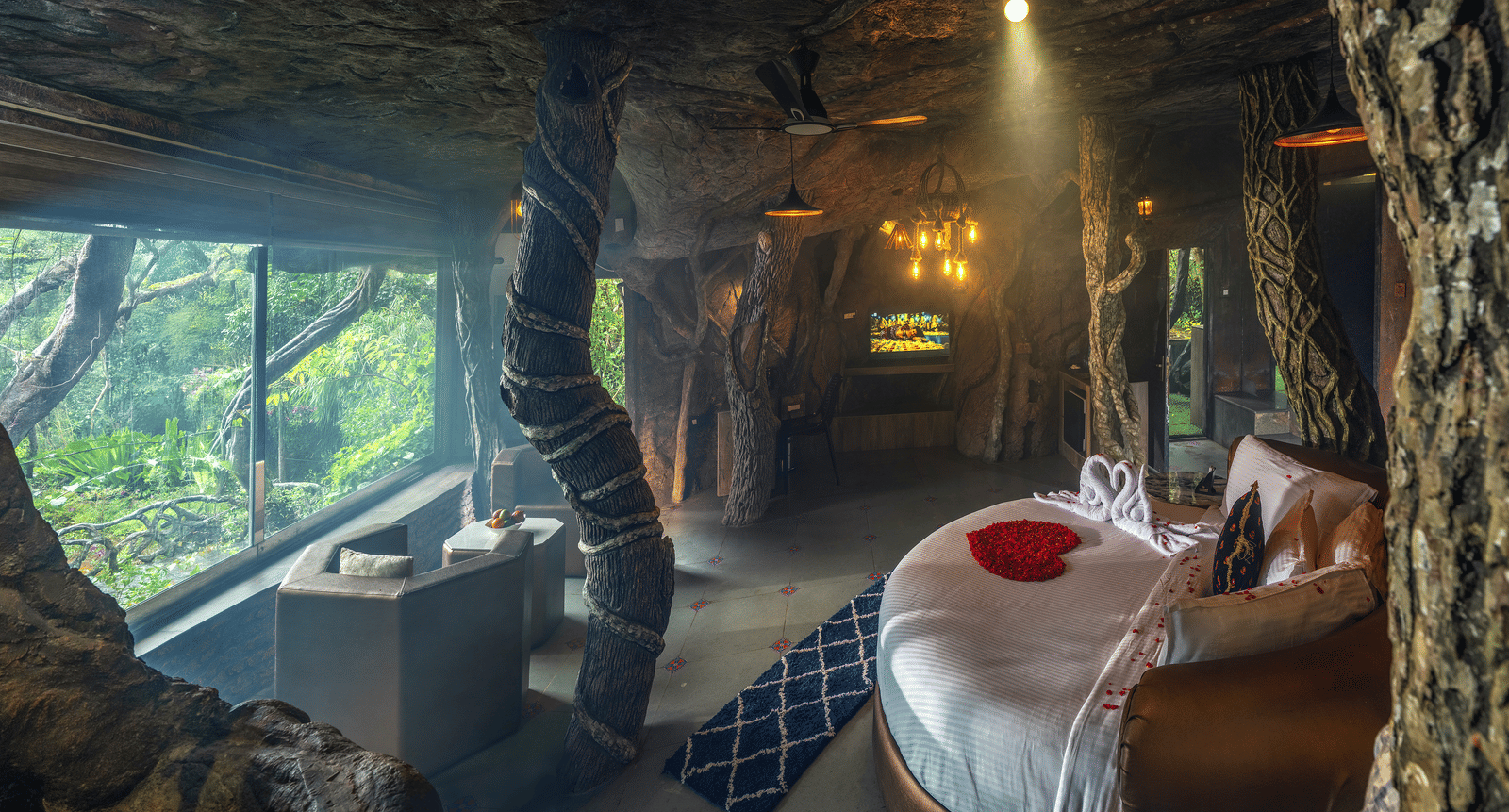 The sleeping area of the Cave Room at Parakkat Nature Hotel and Resorts, Munnar, featuring a large, circular bed, ambient lighting, and walls designed to resemble natural rock formations.