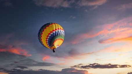 A hot air balloon in view from below with different hues of colours on the clouds above.