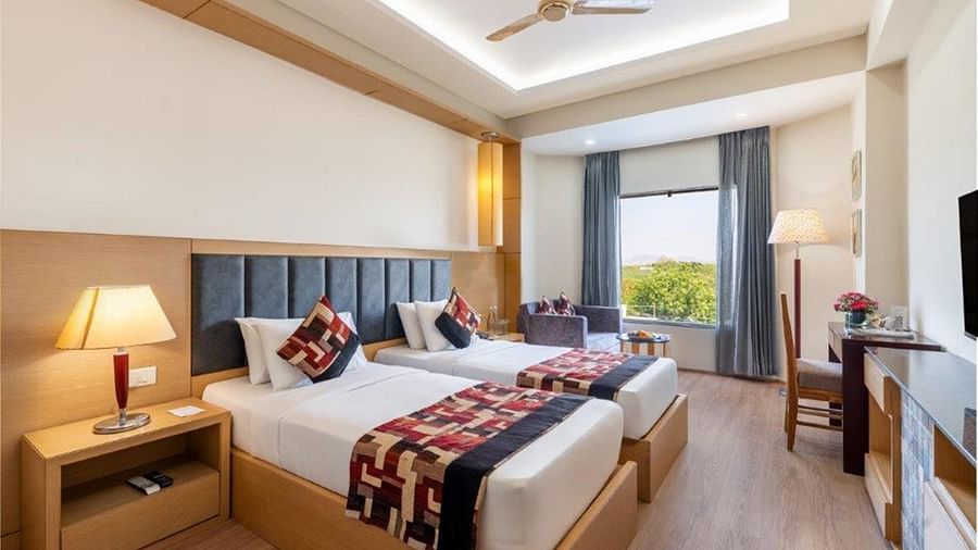 Twin beds, TV, side tables, and ceiling fan in a room at Golden Tulip, Udaipur.