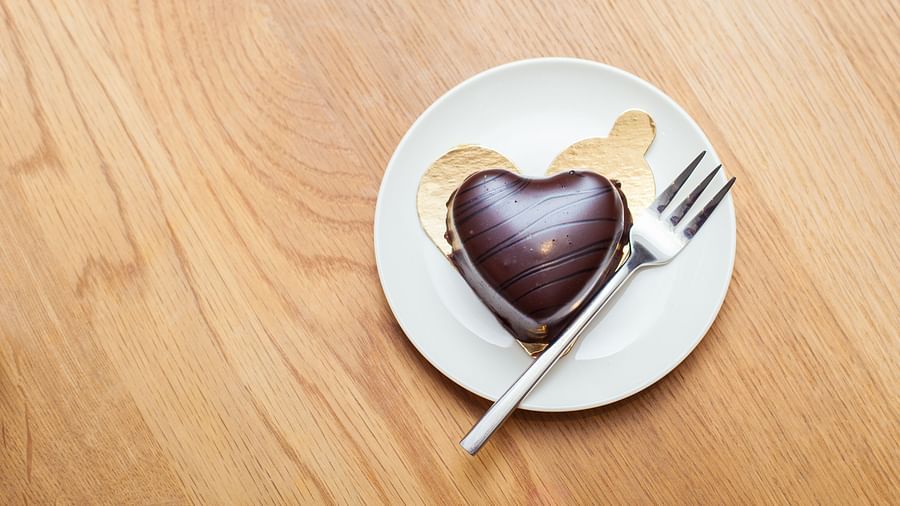 A heart-shaped chocolate dessert with a fork on a white plate on a wooden table| The Shop | Central Mansions, Phnom Penh