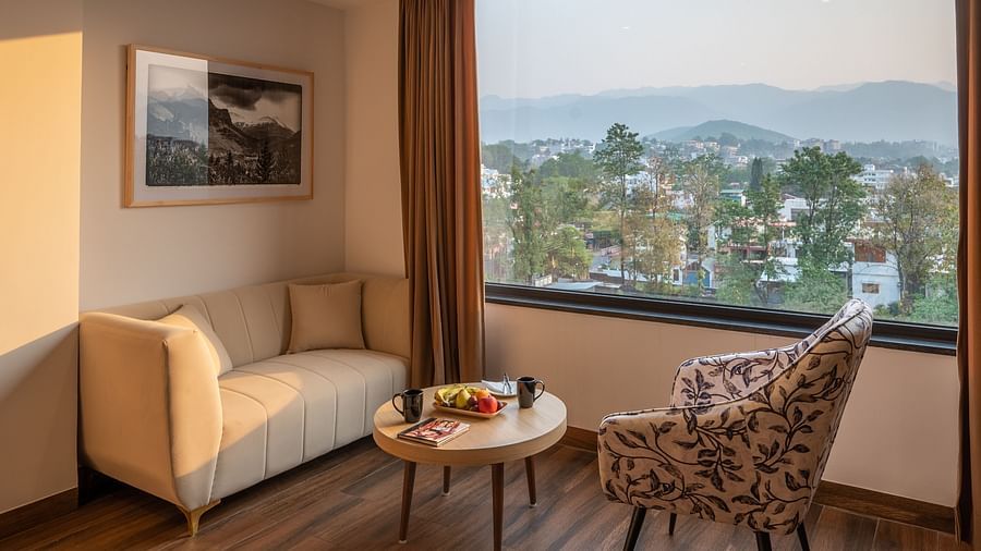 Living area of a suite at Vishranti Hotel, Dehradun Featuring a large window, a sofa, chair and a round table.