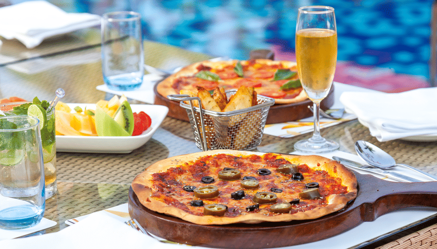 a pizza on a wooden plate kept on the table - Caravela Beach Resort Goa
